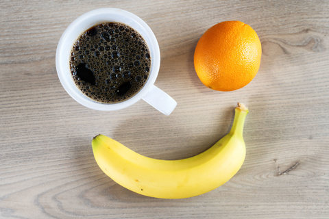 An overhead view of a cup of coffee, an orange, and a banana