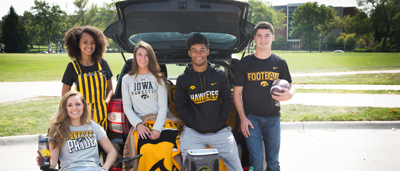 A group of students tailgating and smiling at the camera wearing Hawkeye merchandise