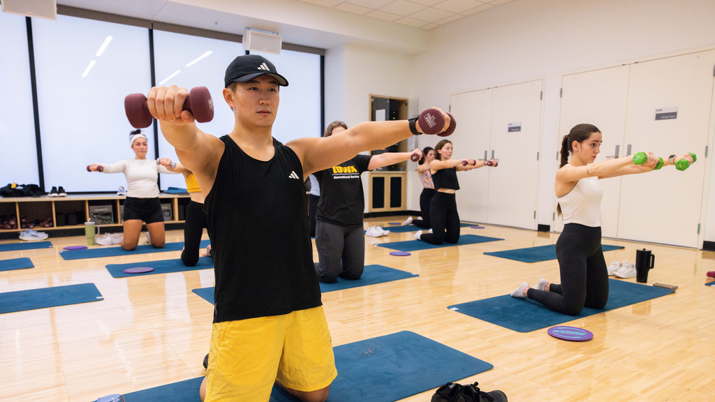Students and trainers practice yoga poses during a mind body group fitness class.
